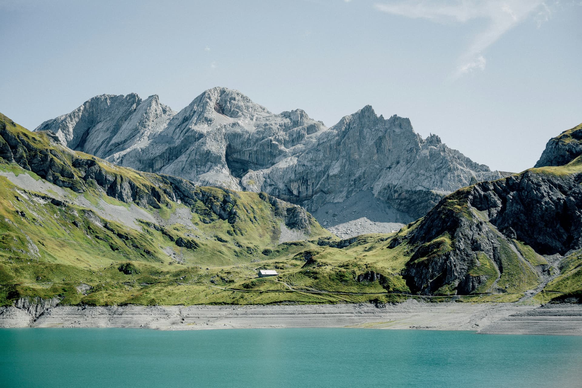 Türkiser Alpsee mit Bergkulisse, Wiesen und kleinem Haus